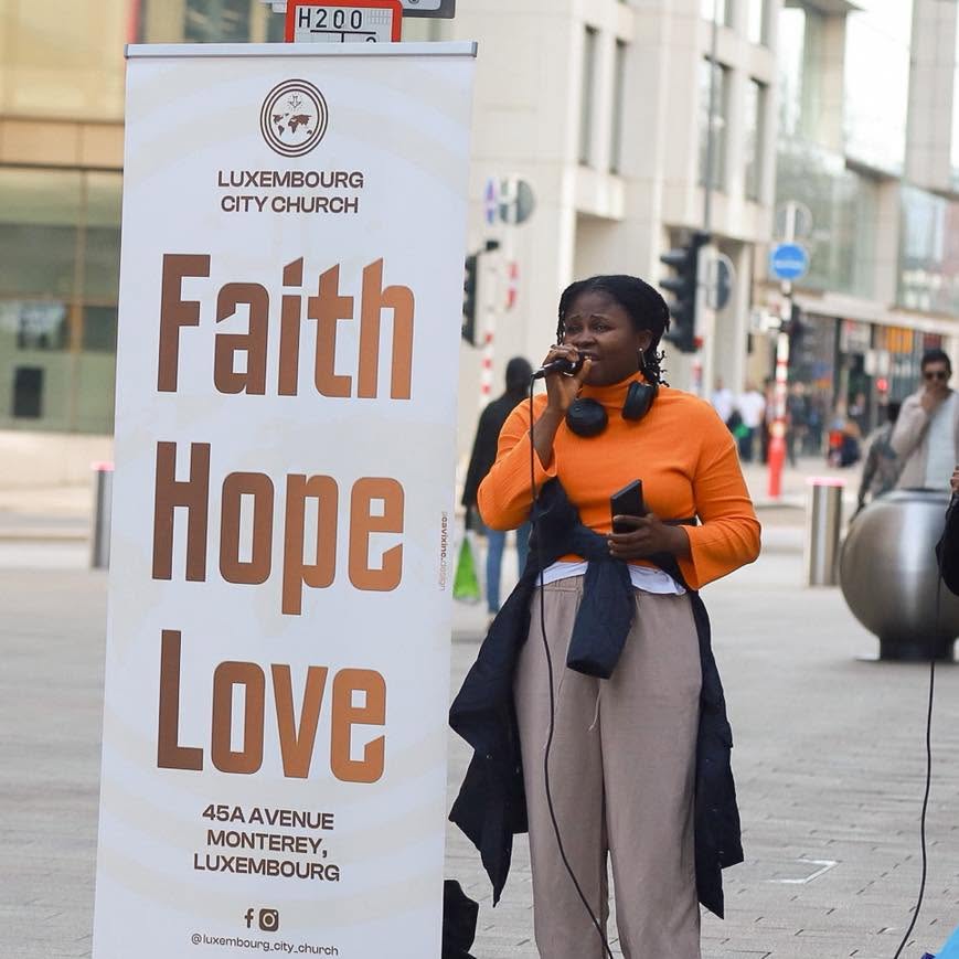 A singer beside the Luxembourg City Church Faith Hope Love banner